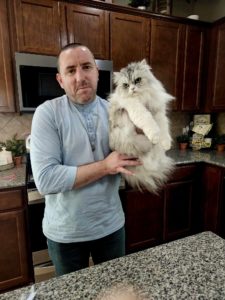Roy Coffey holds up a white longhaired cat who is about to get groomed.